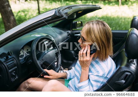 A woman is driving a convertible car. Summer road trip to nature 96664688
