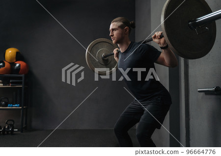 Crossfit athlete lifting barbell in dark gym 96664776