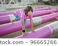 Cute caucasian boy posing in a pink stylish printed t-shirt among pink iron pipes on an industrial background. Fashion style photoshoot 96665266
