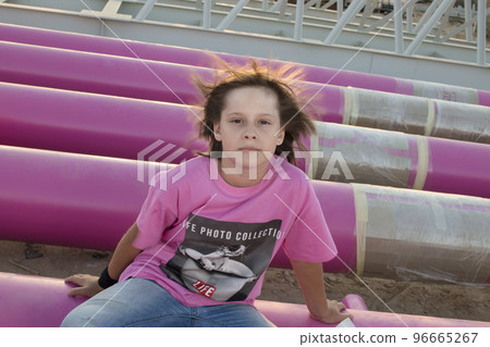 Cute caucasian boy posing in a pink stylish printed t-shirt among pink iron pipes on an industrial background. Fashion style photoshoot Cute caucasian boy posing in a pink stylish printed t-shirt among pink iron pipes on an industrial background. Fashion style photoshoot 96665267