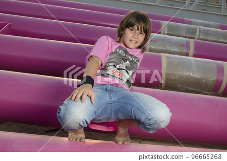 Cute caucasian boy posing in a pink stylish printed t-shirt among pink iron pipes on an industrial background. Fashion style photoshoot Cute caucasian boy posing in a pink stylish printed t-shirt among pink iron pipes on an industrial background. Fashion style photoshoot 96665268