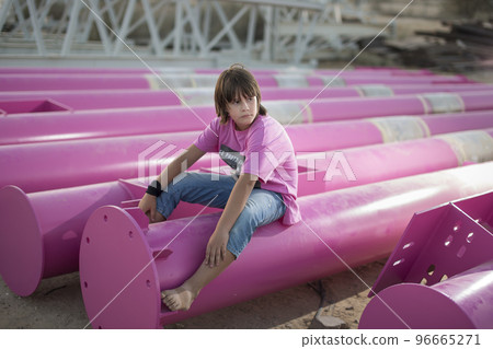 Cute caucasian boy posing in a pink stylish printed t-shirt among pink iron pipes on an industrial background. Fashion style photoshoot Cute caucasian boy posing in a pink stylish printed t-shirt among pink iron pipes on an industrial background. Fashion style photoshoot 96665271