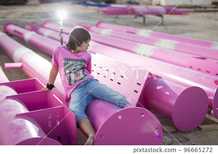 Cute caucasian boy posing in a pink stylish printed t-shirt among pink iron pipes on an industrial background. Fashion style photoshoot Cute caucasian boy posing in a pink stylish printed t-shirt among pink iron pipes on an industrial background. Fashion style photoshoot 96665272