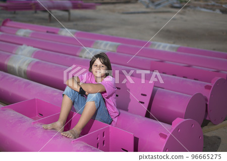 Cute caucasian boy posing in a pink stylish printed t-shirt among pink iron pipes on an industrial background. Fashion style photoshoot 96665275