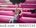 a cute kid in a pink t-shirt with a cat print plays among pink pipes with black clouds, rain, boats and paper planes against the blue sky in an industrial location. fashion style photoshoot 96665334
