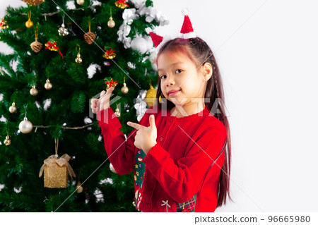 Merry Christmas, asian kid wear red sweater decorating Christmas tree with gift box pine cone silver ball white background. 96665980