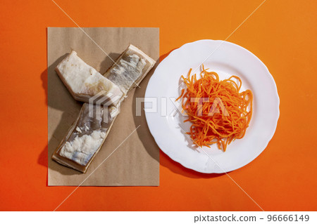 Two pieces of salted bacon and carrots on a white plate on an orange background, top view 96666149
