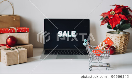 Successful Christmas Season in E-Commerce, Christmas online shopping. Open laptop computer Display screen, mini shopping cart, Poinsettias Christmas Flower and gift boxes on white table Successful Christmas Season in E-Commerce, Christmas online shopping. Open laptop computer Display screen, mini shopping cart, Poinsettias Christmas Flower and gift boxes on white table 96666343