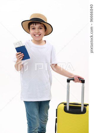 Happy preteen child passenger, teenager traveler boy in casual t-shirt, blue jeans and straw hat, going on summer holidays, walks with boarding pass, air ticket and yellow suitcase on white background 96666840