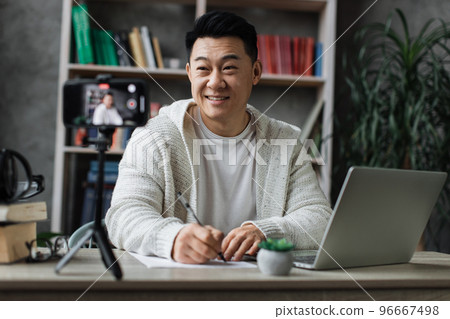 Focus on screen, smiling asian man talking and gesturing in front of modern smartphone camera 96667498