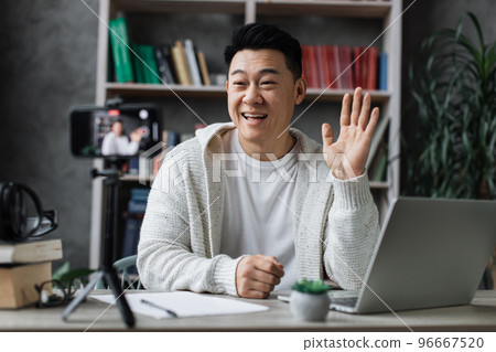 Attractive asian man in casual clothes talking and gesturing while recording video on modern phone Attractive asian man in casual clothes talking and gesturing while recording video on modern phone 96667520
