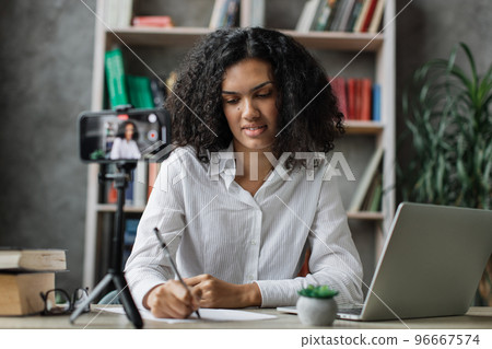 Charming multinational woman in white shirt talking with subscribers while writing report 96667574