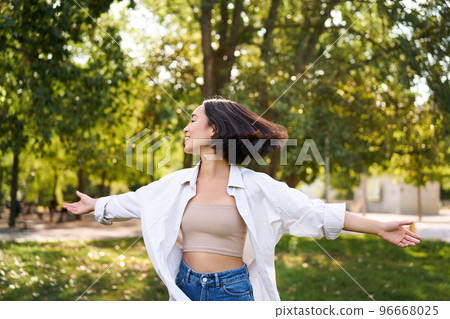 Freedom and people concept. Happy young asian woman dancing in park around trees, smiling and enjoying herself 96668025