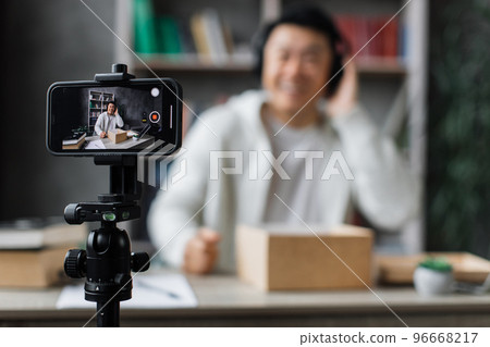 Focuse on smartphone screen, asian man recording video on phone camera while unpacking box 96668217