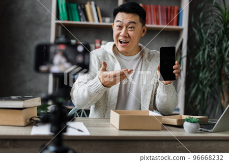 Pleasant asian man opening parcel box with new smartphone Pleasant asian man opening parcel box with new smartphone 96668232