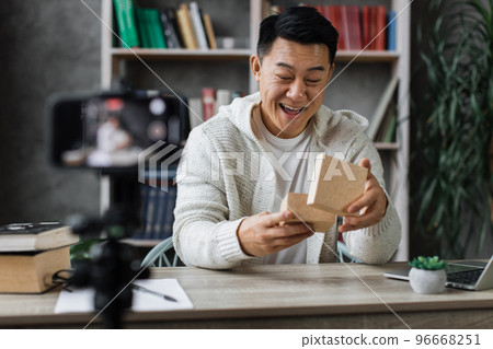 Handsome asian man in casual wear recording video on camera while unpacking gift box. Handsome asian man in casual wear recording video on camera while unpacking gift box. 96668251