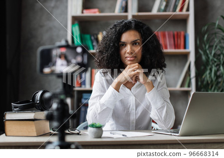 Smiling female teacher sitting at desk with books and notes. 96668314