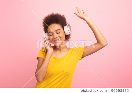 Satisfied relaxed young african american curly woman in casual, wireless headphones, dancing, enjoy music 96668383