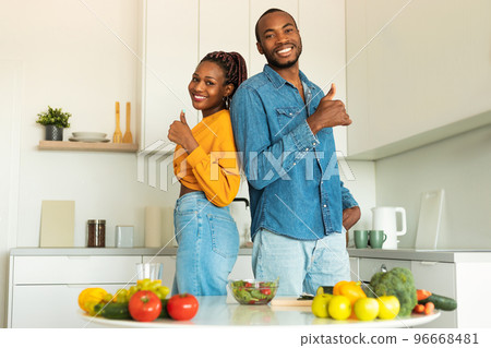Excited black couple making healthy vegan salad with many vegetables in modern kitchen and showing thumbs up 96668481