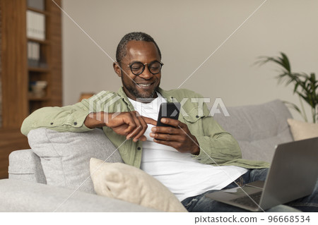Glad middle aged african american man in glasses reads message on phone, watches video surfing in room 96668534