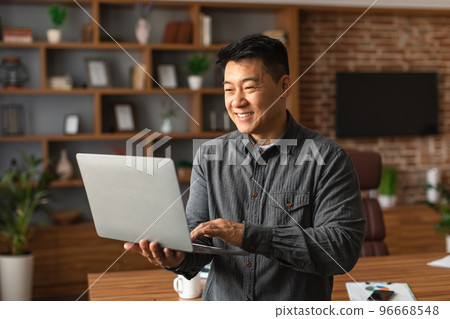 Smiling handsome middle aged asian man ceo manager typing on laptop, has video call at home office interior Smiling handsome middle aged asian man ceo manager typing on laptop, has video call at home office interior 96668548