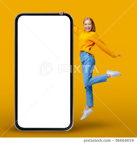 Cheerful Young Woman Jumping Near Big Smartphone With Blank White Screen Cheerful Young Woman Jumping Near Big Smartphone With Blank White Screen 96668659