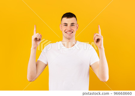 Happy caucasian man in white t-shirt pointing up at empty space and smiling at camera, standing over yellow background Happy caucasian man in white t-shirt pointing up at empty space and smiling at camera, standing over yellow background 96668660