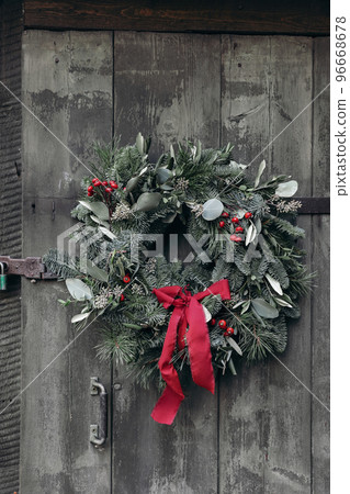 Christmas home decor. Natural advent wreath. Floral garland of fir, pine tree branches. Olive, eucalyptus leaves with red berries. Shabby wooden green door textured background. Vertical, no people. 96668678