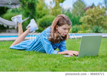 Preteen girl lying on grass in backyard using laptop for relaxing and studying 96669721