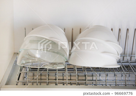 Bright clean and washed glass and ceramic bowls on metal rack inside kitchen cupboard. Modern kitchen with tableware drying. Bright clean and washed glass and ceramic bowls on metal rack inside kitchen cupboard. Modern kitchen with tableware drying. 96669776