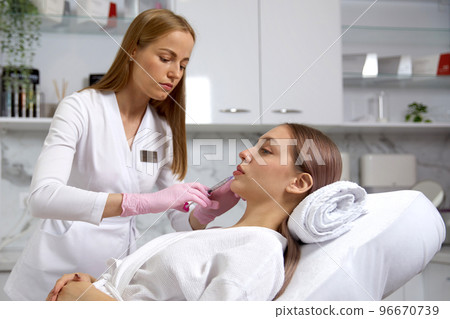 Rejuvenating facial injections procedure for lips of a beautiful, young woman 96670739