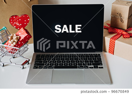 Valentines Day Sale Successful. Valentines Day Online shopping, E-Commerce. Open laptop computer Display screen, mini shopping cart, shopping bags with heart and gift boxes on white table. 96670849