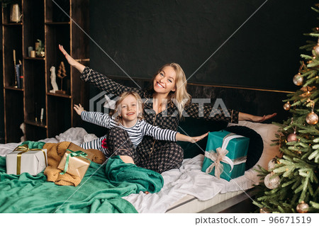 Mom and daughter are sitting in pajamas on the bed 96671519