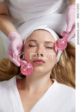 Young woman receiving facial massage with glass balls in beauty salon Young woman receiving facial massage with glass balls in beauty salon 96671950
