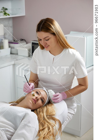 Cosmetologist applying a mask from clay to the face of a beautiful woman. Spa treatment and face care in the beauty salon 96671983