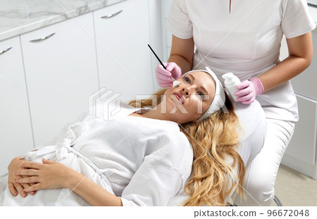 Cosmetologist applying a clay mask to the face of beautiful woman. Spa treatment and face care in the beauty salon 96672048