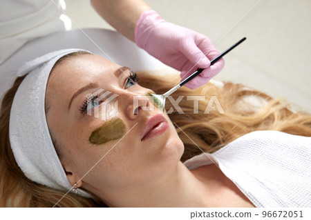 Cosmetologist applying a clay mask to the face of beautiful woman. Spa treatment and face care in the beauty salon Cosmetologist applying a clay mask to the face of beautiful woman. Spa treatment and face care in the beauty salon 96672051
