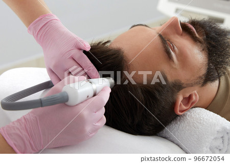 Doctor female dermatologist trichologist makes a procedure to stimulate hair growth on head to a patient man Doctor female dermatologist trichologist makes a procedure to stimulate hair growth on head to a patient man 96672054
