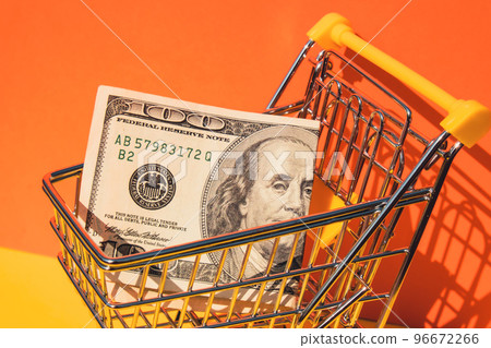 US dollar paper currency 100 banknote money Shopping trolley cart on colorful orange yellow background. Copy space for your text. Online shopping, buy mall market shop consumer concept. Small toy 96672266