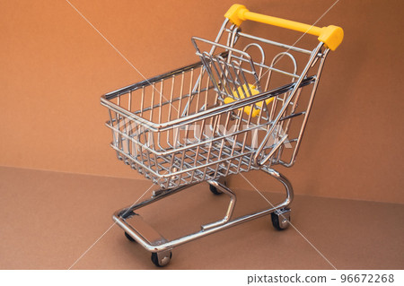 Empty shopping trolley cart on beige background. Copy space for your text. Online shopping, buy mall market shop consumer concept. Small toy supermarket grocery push cart. Food crisis. Rising food 96672268