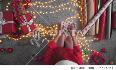 Girl creates New Year's packages with red paper, colored ribbons. A young woman is packing Christmas 96673861