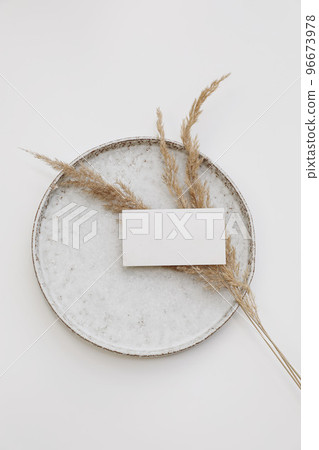 Blank textured paper business card mockup. Ceramic plate isolated on white table background. Boho stationery with dry grass. Branding template. Minimal composition. Vertical flat lay, top view. Blank textured paper business card mockup. Ceramic plate isolated on white table background. Boho stationery with dry grass. Branding template. Minimal composition. Vertical flat lay, top view. 96673978