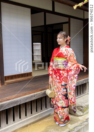A woman in a kimono standing on the porch of an old folk house 96674012