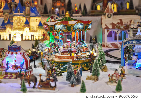 Cheerful miniature carousel with toy people in winter park during Christmas market. Miniature toy city during the winter season. City scene in miniature models 96676556