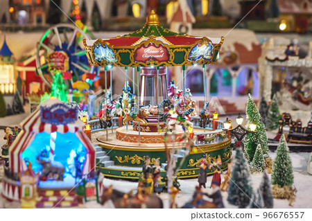 Cheerful miniature carousel with toy people in winter park during Christmas market. Miniature toy city during the winter season. City scene in miniature models 96676557