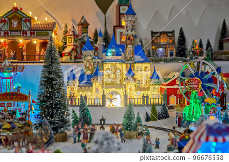 Miniature castle, ferris wheel and carousel with toy people in winter park during Christmas market. Miniature toy city during the winter season. City scene in miniature models Miniature castle, ferris wheel and carousel with toy people in winter park during Christmas market. Miniature toy city during the winter season. City scene in miniature models 96676558