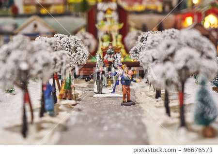 Miniature figures of man in tuxedo and lady in dress, coachman and carriage in miniature winter park. Miniature toy city during winter season. City scene in miniature models 96676571