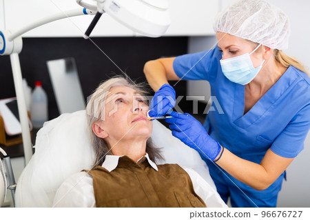 Qualified cosmetologist giving beauty injections to elderly female client 96676727