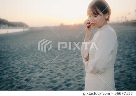 Photo of a woman making a phone call on the beach at sunset 96677135