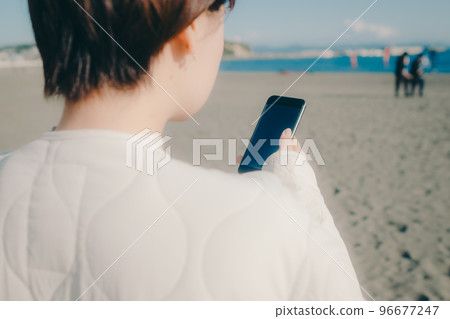 一位女士在海灘上拿著智能手機的照片 96677247